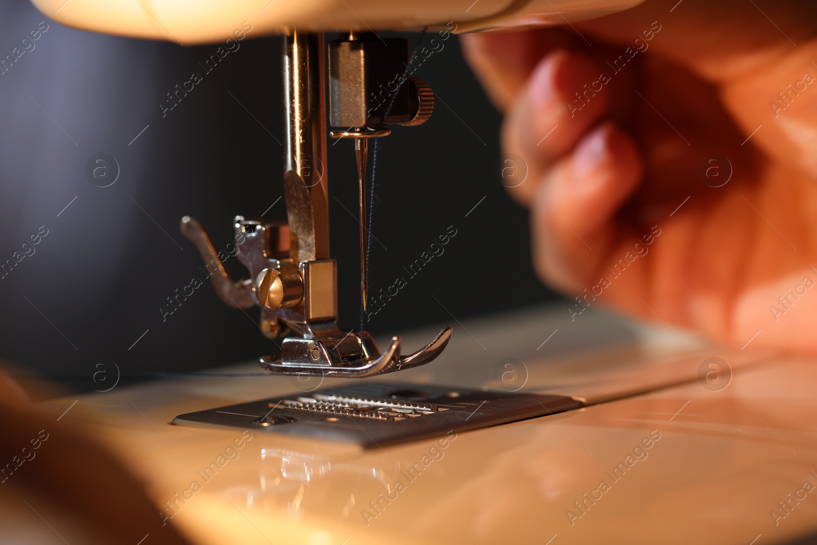 Photo of Woman working with sewing machine on blurred grey background, macro view