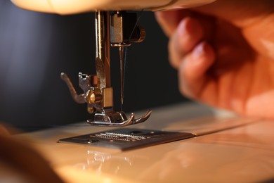 Photo of Woman working with sewing machine on blurred grey background, macro view