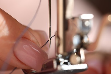 Photo of Woman threading sewing machine needle on blurred background, macro view