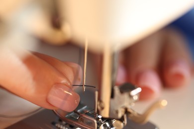 Photo of Woman threading sewing machine needle on blurred background, macro view