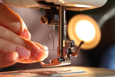 Photo of Woman threading sewing machine needle on blurred background, macro view