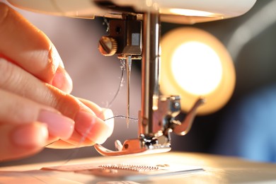 Photo of Woman threading sewing machine needle on blurred background, macro view