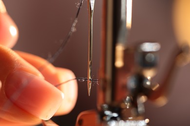 Photo of Woman threading sewing machine needle on blurred grey background, macro view