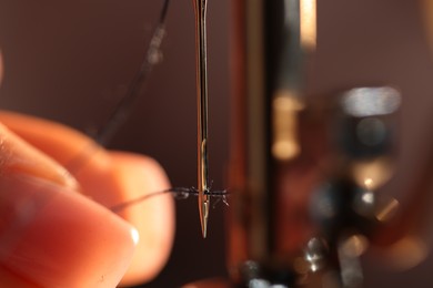 Photo of Woman threading sewing machine needle on blurred grey background, macro view