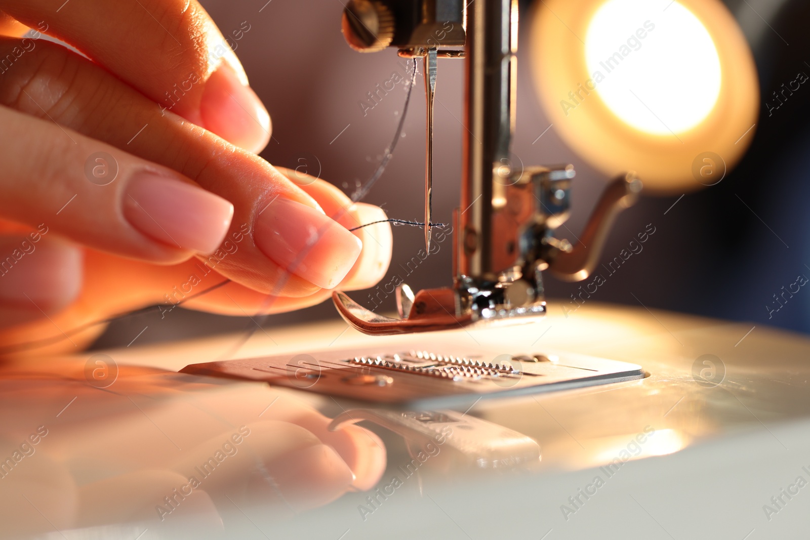 Photo of Woman threading sewing machine needle on blurred grey background, macro view