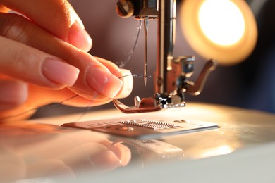 Photo of Woman threading sewing machine needle on blurred grey background, macro view