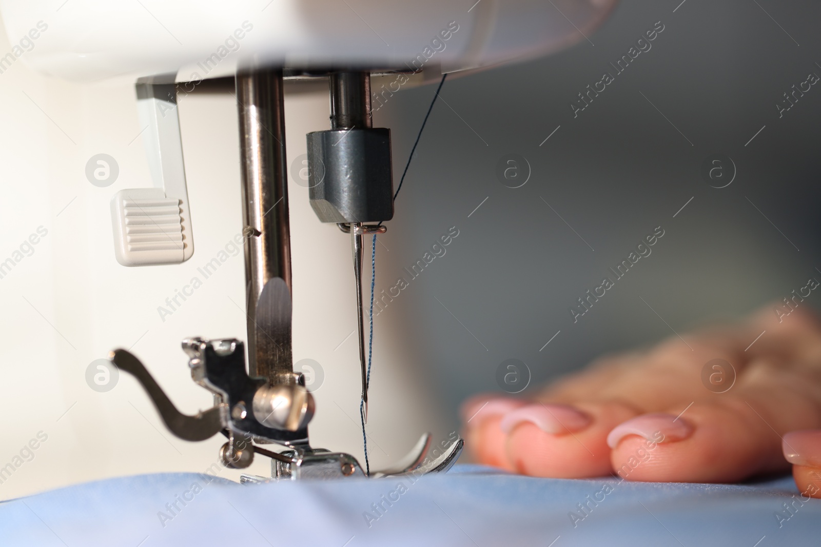 Woman working with sewing machine on blurred grey background, macro view Photo of Woman working with sewing machine on blurred grey background, macro view