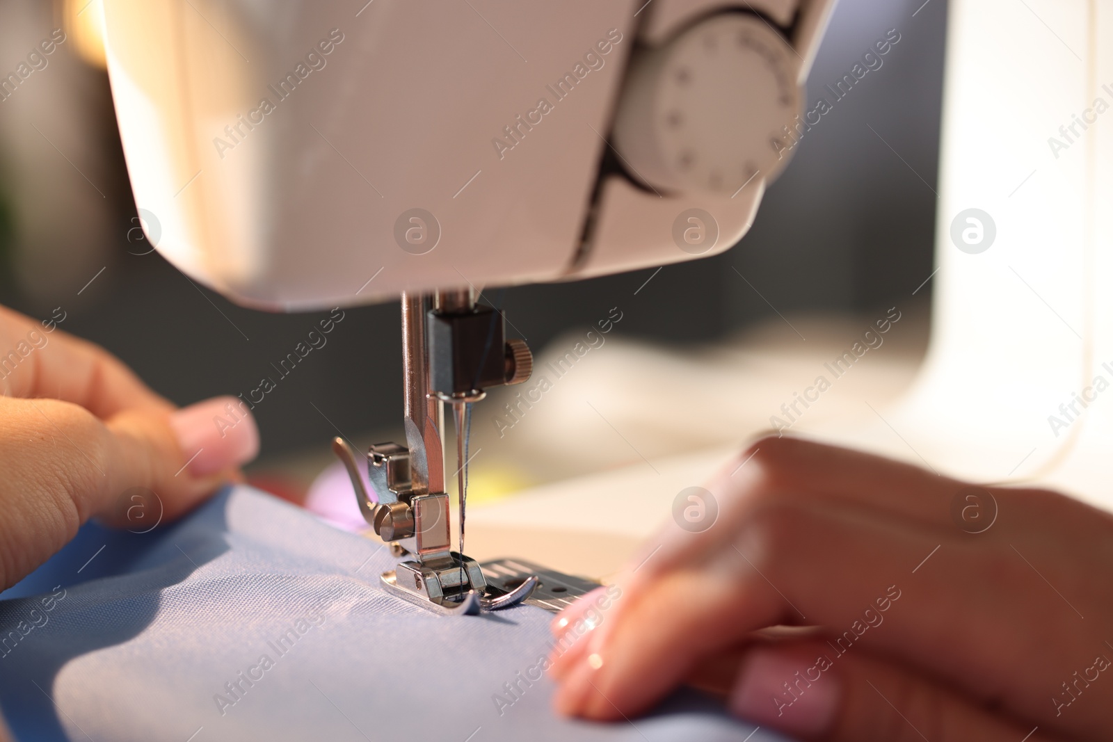 Woman working with sewing machine on blurred grey background, macro view Photo of Woman working with sewing machine on blurred grey background, macro view