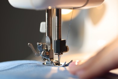 Photo of Woman working with sewing machine on blurred grey background, macro view