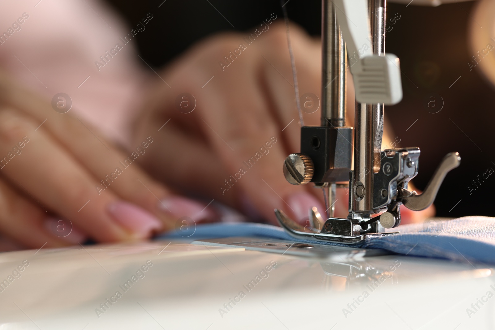 Woman working with sewing machine on blurred dark background, macro view Photo of Woman working with sewing machine on blurred dark background, macro view