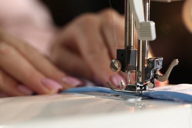 Photo of Woman working with sewing machine on blurred dark background, macro view