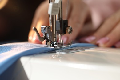 Photo of Woman working with sewing machine on blurred dark background, macro view