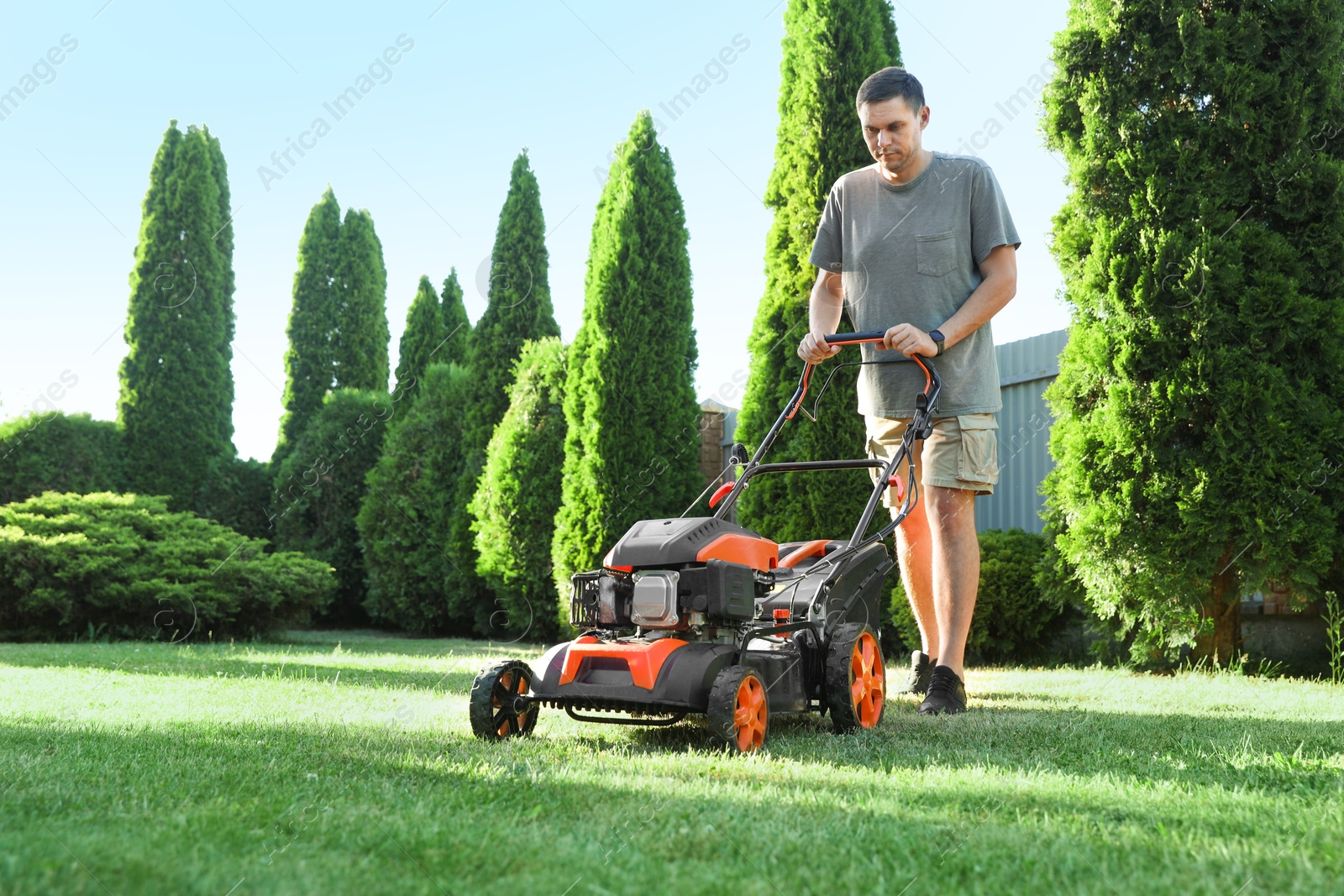 Man cutting green grass with lawn mower in garden, space for text Photo of Man cutting green grass with lawn mower in garden, space for text