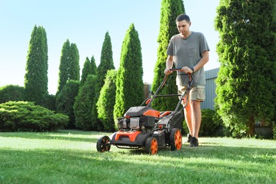 Photo of Man cutting green grass with lawn mower in garden, space for text