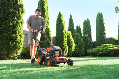 Photo of Man cutting green grass with lawn mower in garden, space for text