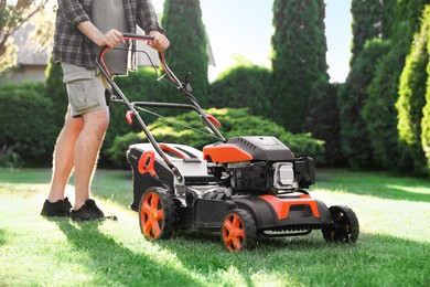 Photo of Man cutting green grass with lawn mower in garden, closeup