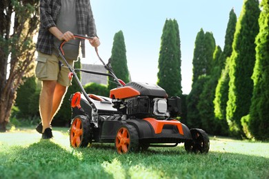 Photo of Man cutting green grass with lawn mower in garden, closeup