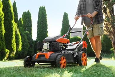 Photo of Man cutting green grass with lawn mower in garden, closeup