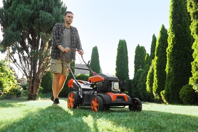 Photo of Man cutting green grass with lawn mower in garden, low angle view
