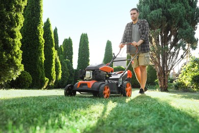 Photo of Man cutting green grass with lawn mower in garden, low angle view