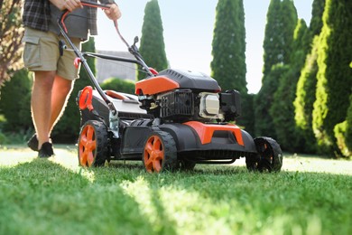 Photo of Man cutting green grass with lawn mower in garden, closeup