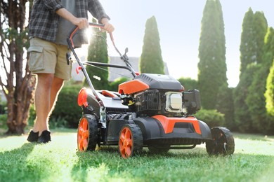 Photo of Man cutting green grass with lawn mower in garden, closeup