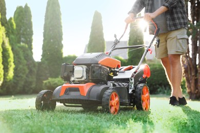 Photo of Man cutting green grass with lawn mower in garden, closeup