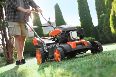 Photo of Man cutting green grass with lawn mower in garden, closeup
