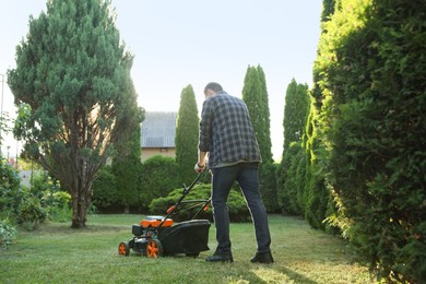 Photo of Man cutting green grass with lawn mower in garden