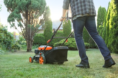 Photo of Man cutting green grass with lawn mower in garden, closeup