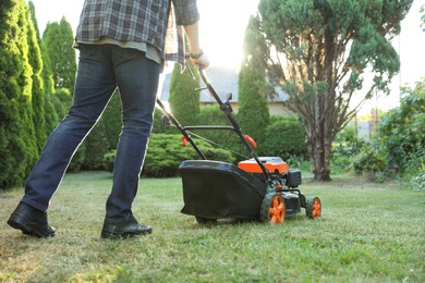 Photo of Man cutting green grass with lawn mower in garden, closeup