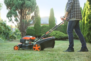 Photo of Man cutting green grass with lawn mower in garden, closeup