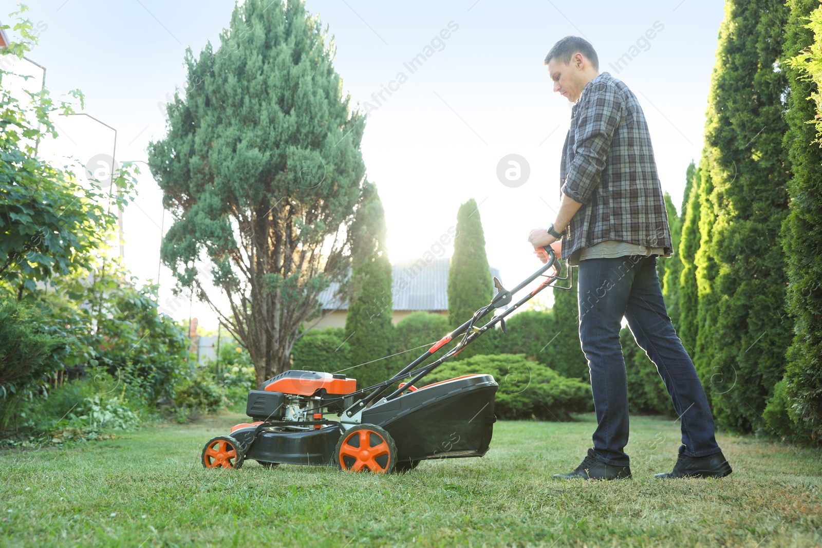Photo of Man cutting green grass with lawn mower in garden