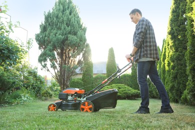Photo of Man cutting green grass with lawn mower in garden