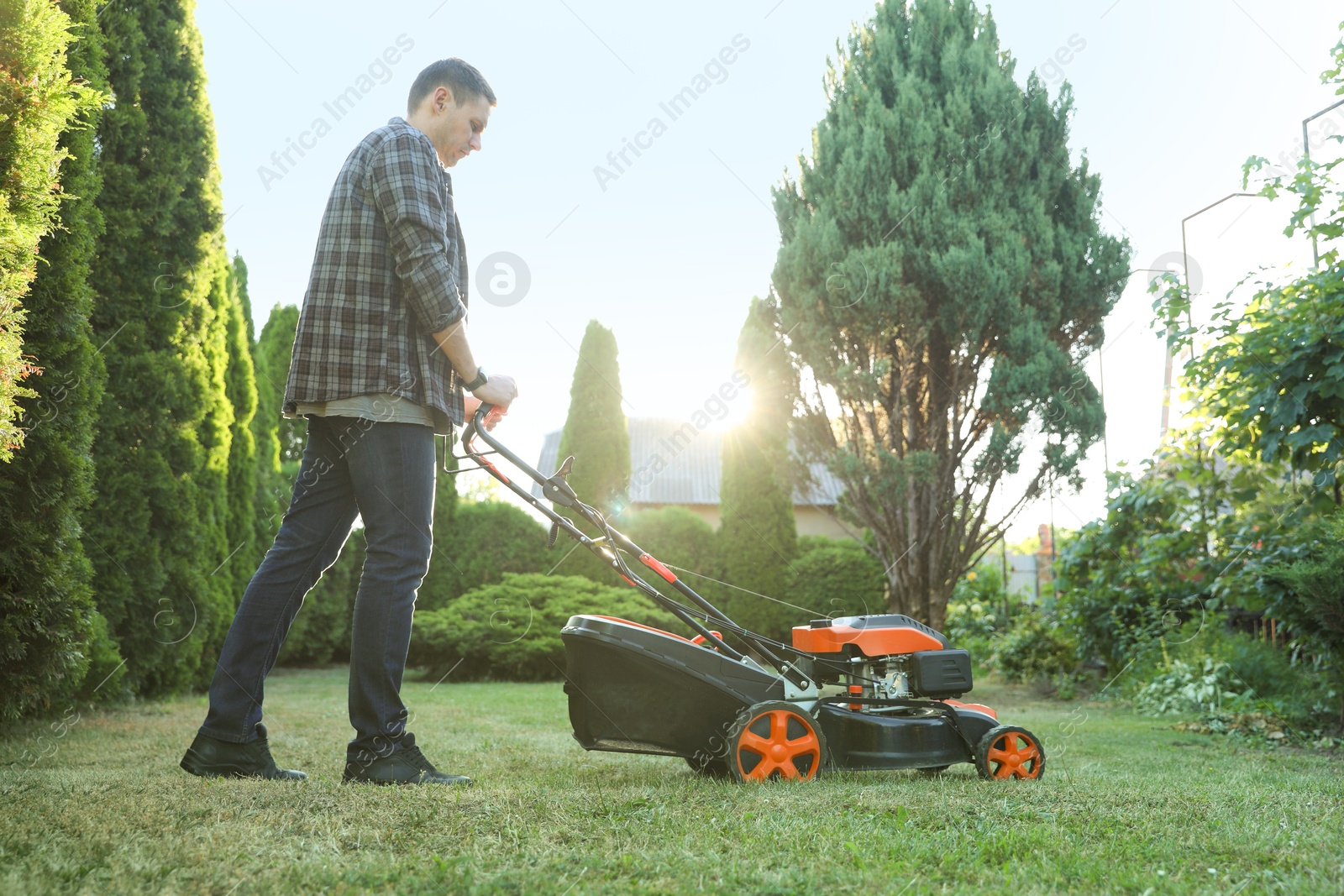 Photo of Man cutting green grass with lawn mower in garden