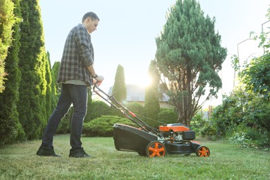 Photo of Man cutting green grass with lawn mower in garden