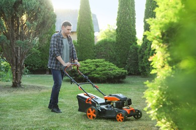 Photo of Man cutting green grass with lawn mower in garden