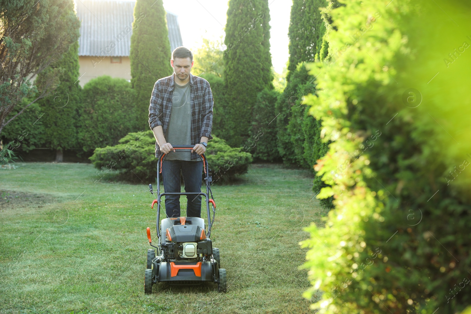 Photo of Man cutting green grass with lawn mower in garden