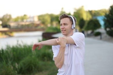 Photo of Smiling sportsman in headphones doing morning exercise outdoors