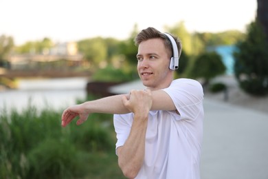 Photo of Smiling sportsman in headphones doing morning exercise outdoors