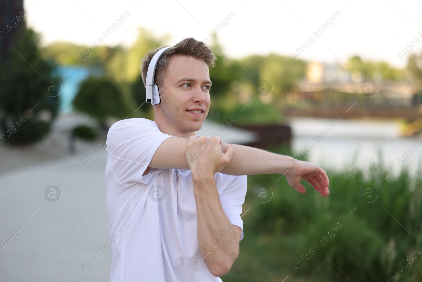 Smiling sportsman in headphones doing morning exercise outdoors Photo of Smiling sportsman in headphones doing morning exercise outdoors