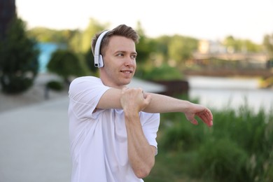 Photo of Smiling sportsman in headphones doing morning exercise outdoors