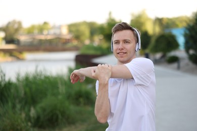 Photo of Smiling sportsman in headphones doing morning exercise outdoors. Space for text