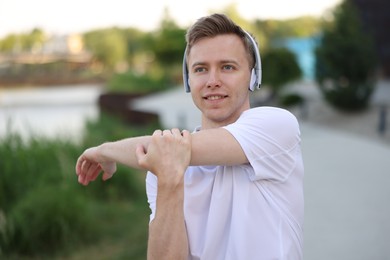 Photo of Smiling sportsman in headphones doing morning exercise outdoors