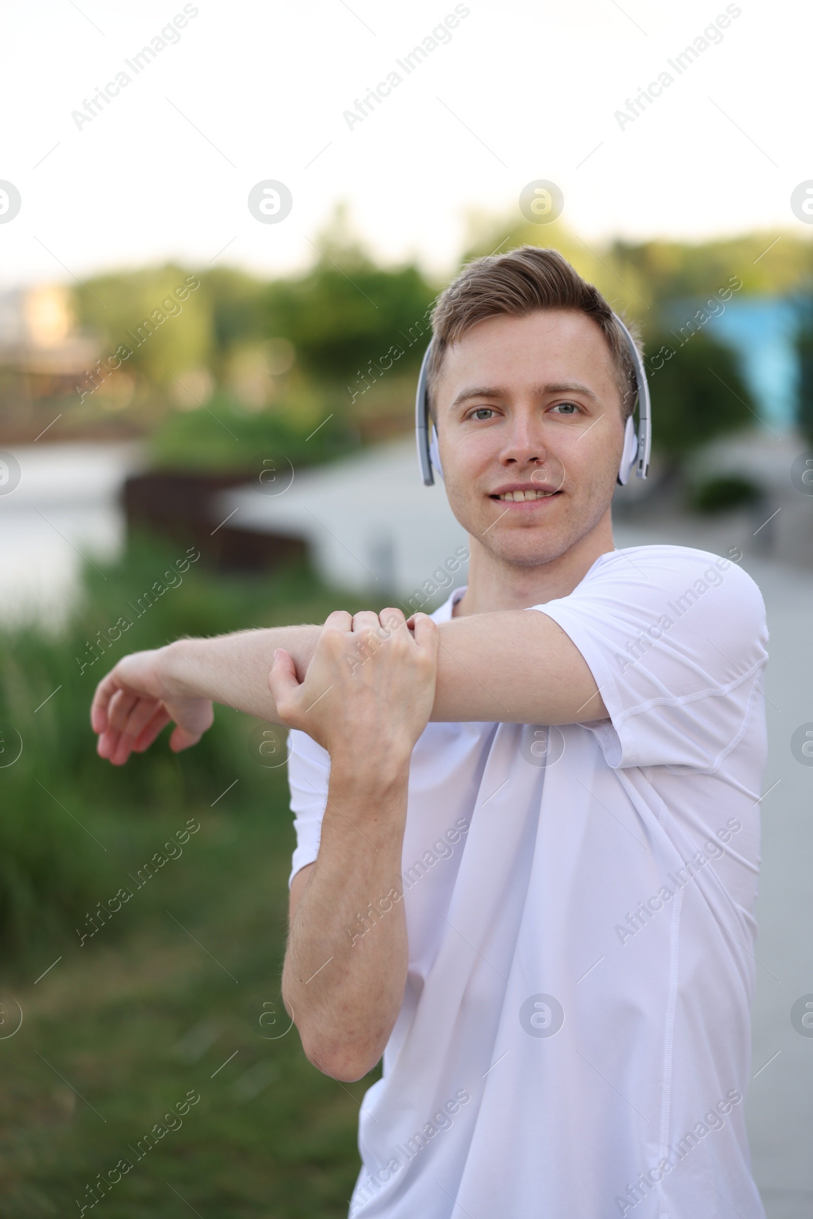 Smiling sportsman in headphones doing morning exercise outdoors Photo of Smiling sportsman in headphones doing morning exercise outdoors