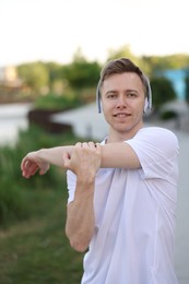 Photo of Smiling sportsman in headphones doing morning exercise outdoors