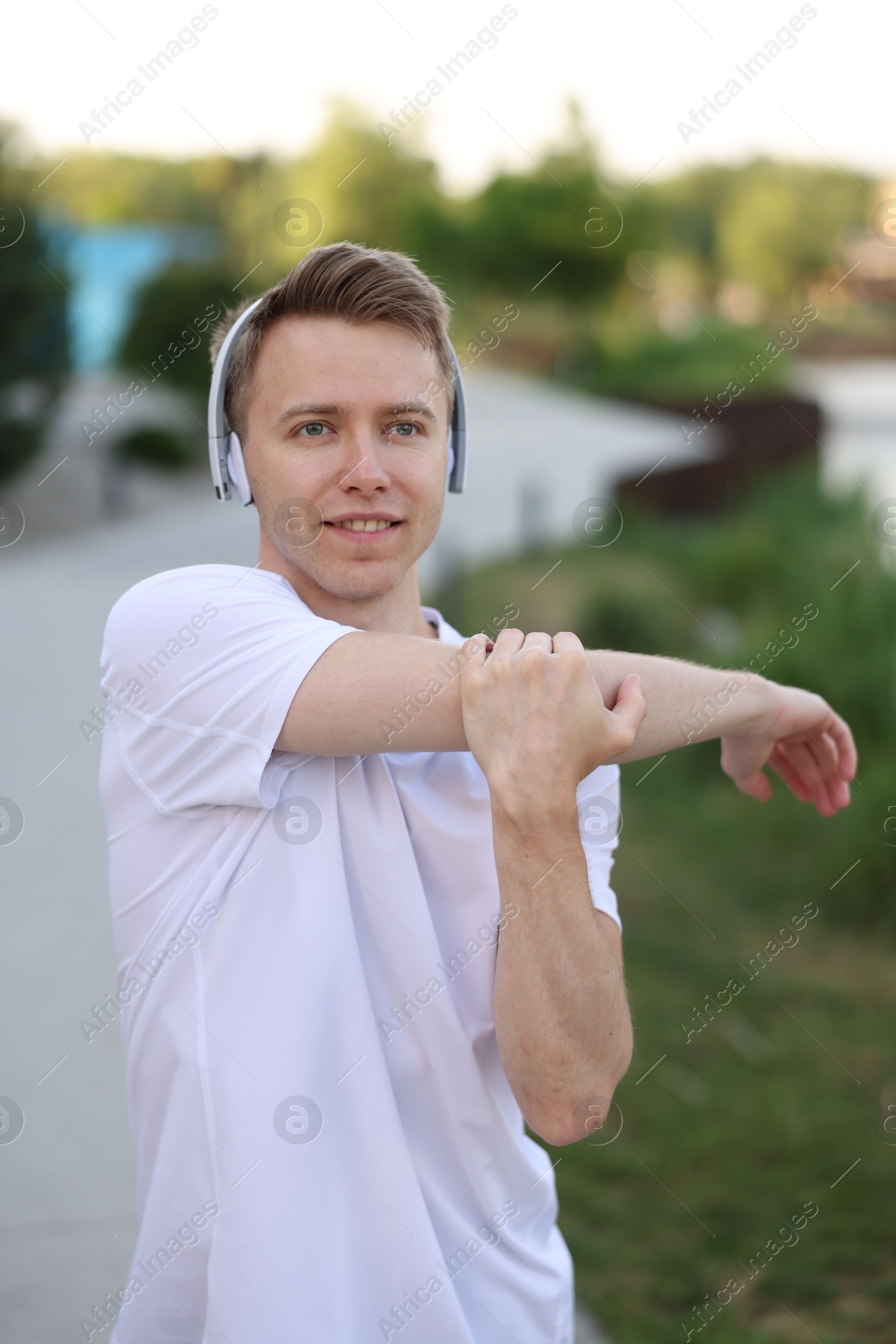 Smiling sportsman in headphones doing morning exercise outdoors Photo of Smiling sportsman in headphones doing morning exercise outdoors