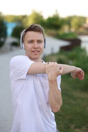 Photo of Smiling sportsman in headphones doing morning exercise outdoors