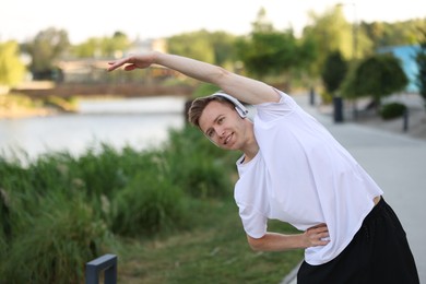 Photo of Smiling sportsman in headphones doing morning exercise outdoors