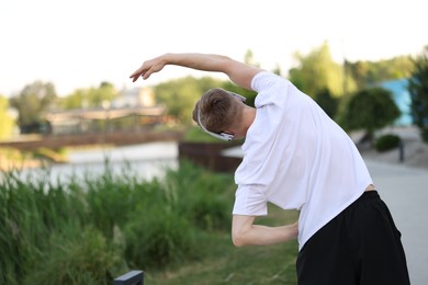 Photo of Sportsman in headphones doing morning exercise outdoors, back view